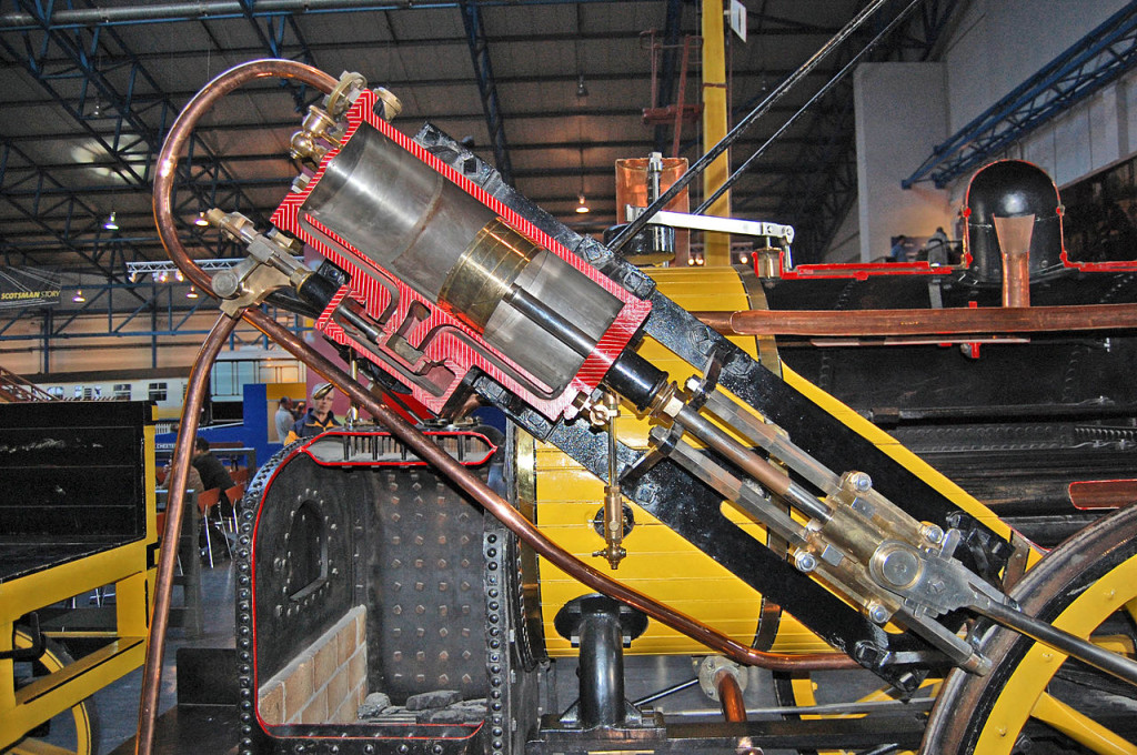 In this cutaway view of the restored Rocket, you can see how the piston and cylinder connect to a shaft that drives the wheel. The black firebox in the background heated water in the boiler. (Wikipedia Commons / Swinsto101)